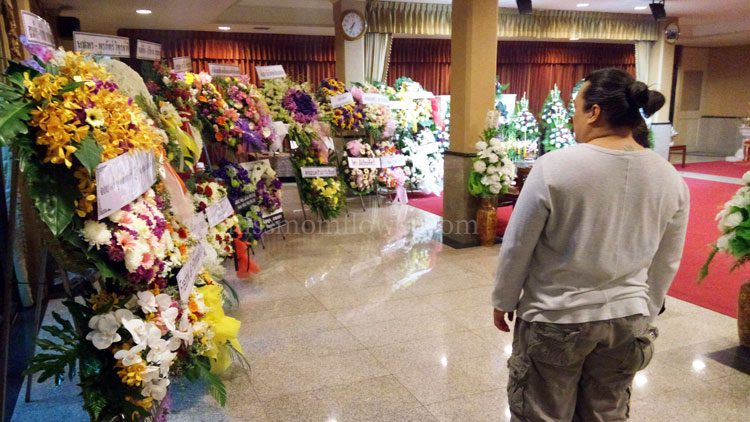 รูปพวงหรีดที่วางในศาลางานศพ และมีเจ้าภาพยืนมองพวงหรีด